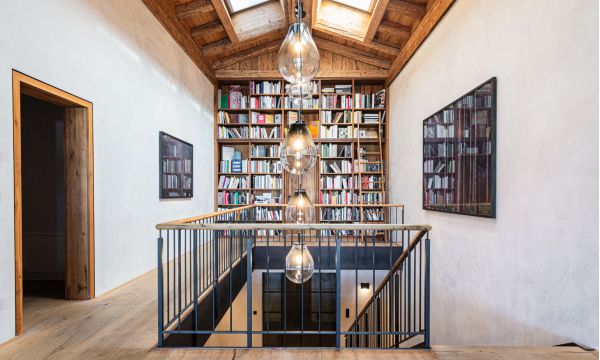 offener, lichtdurchfluteter Treppenaufgang in das Dachgeschoß eines Wohnhauses am Tegernsee mit großer Bücherwand und mit mineralischen Putz an den Wänden, farblich harmonisch abgestimmt