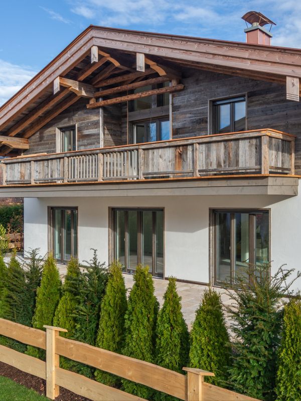 Außenansicht eines alpenländischen Neubaus am Tegernsee mit von Maler Monti gestrichenem Erdgeschoss und Altholzfassade am Dachgeschoß