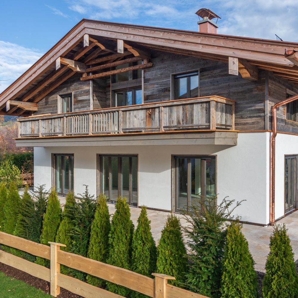 Außenansicht eines alpenländischen Neubaus am Tegernsee mit weißem Anstrich von Maler Monti und Altholzelementen